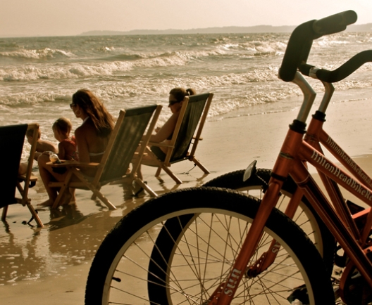 Two bikes parked on a beach with a family in beach chairs in the background
