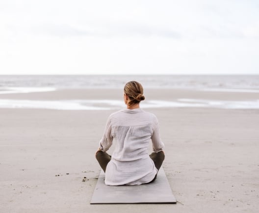 A woman meditating on a beach looking out over the water