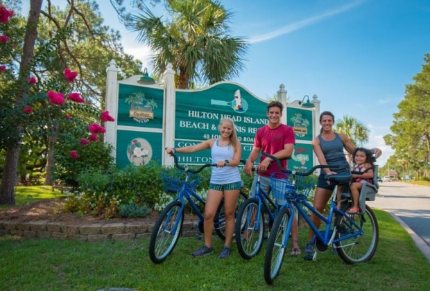 Family of four poses with their bicycles in front of the Hilton Head signage