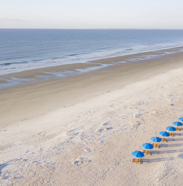 chairs with blue umbrellas lined up on a white sand beach