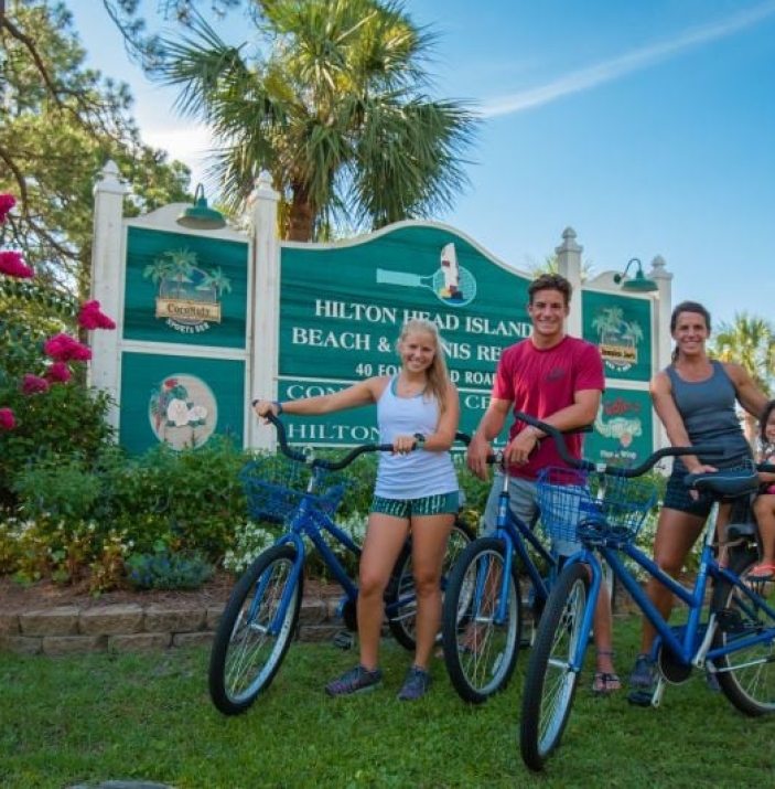 Family of four poses with their bicycles in front of the Hilton Head signage