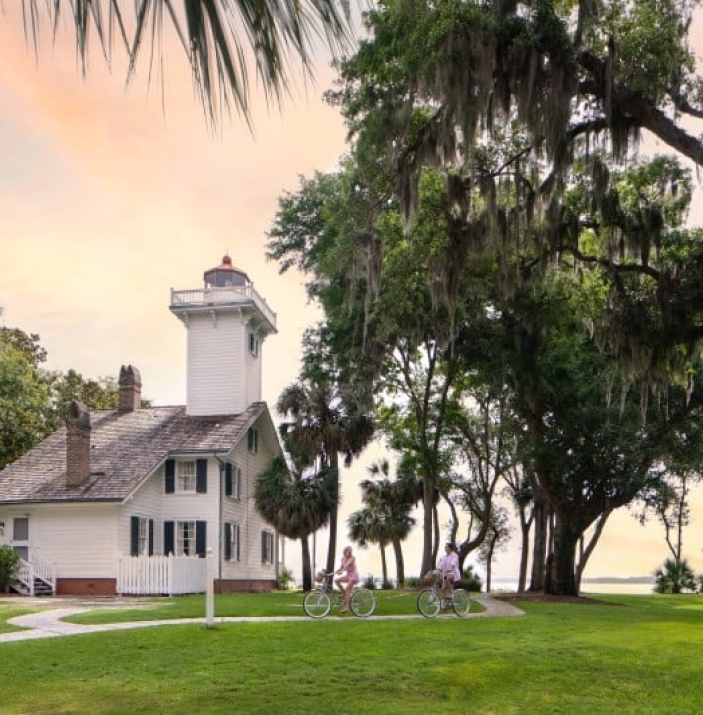Bicyclists ride in front of a lighthouse
