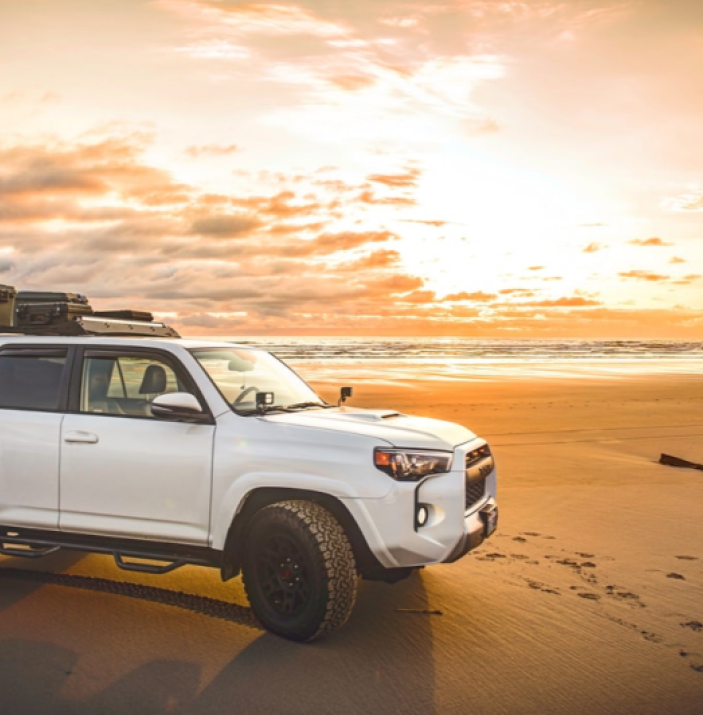 White SUV parked on beach at sunset